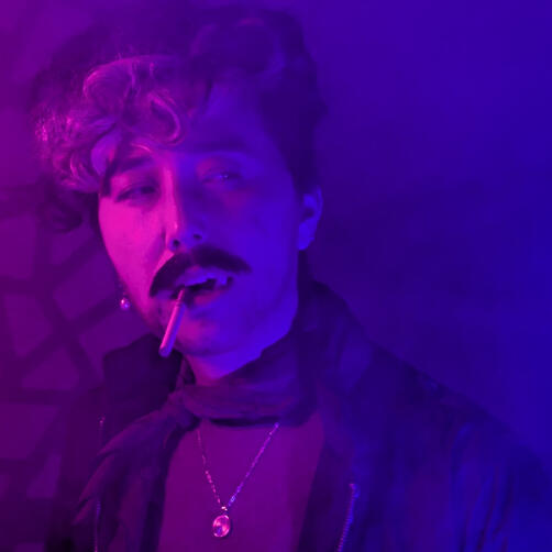 Marrok Cai dressed as Marrok from The Doomsayers on Taino Tales. Their hair is curled and swept to the side. They have a heavy moustache. They are bathed in pink and purple light.
