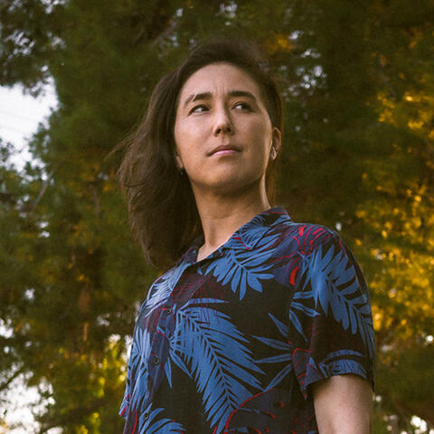 Cai standing in front of a sunlit tree.